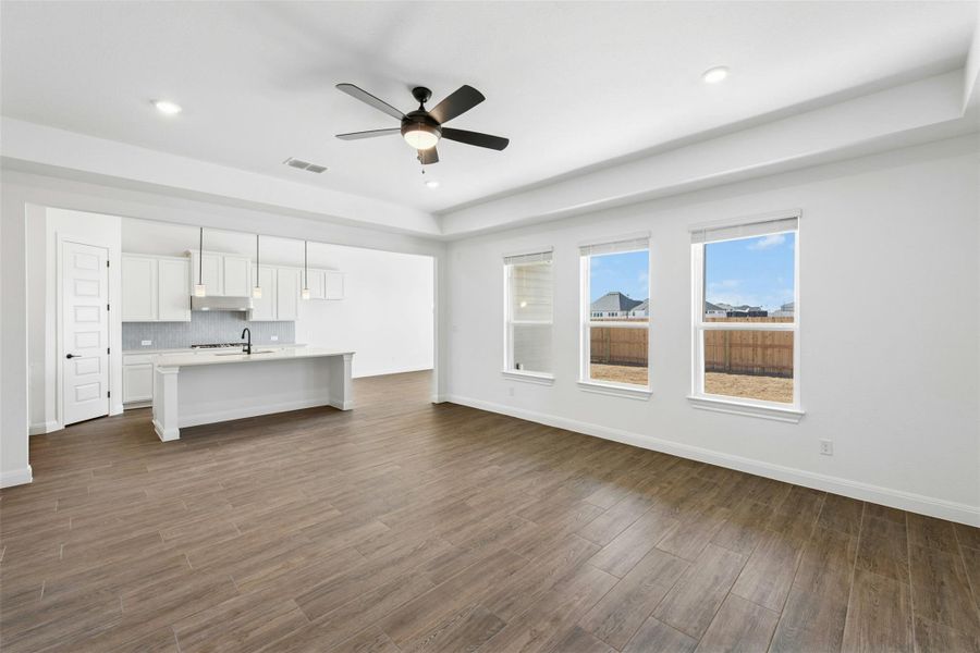 Unfurnished living room with ceiling fan, dark wood-style floors, a tray ceiling, and recessed lighting