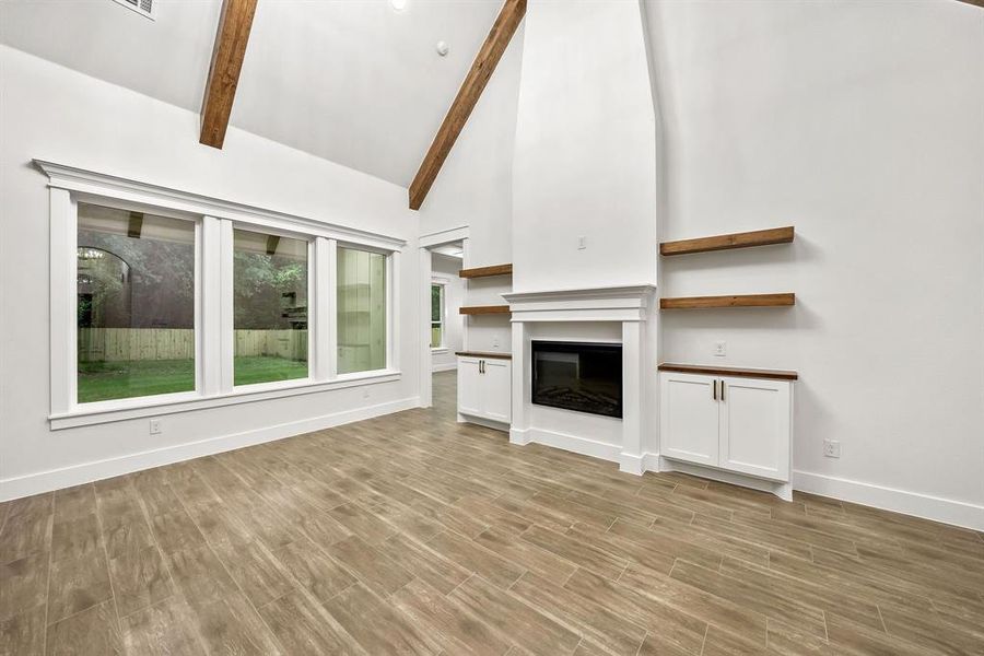 Vaulted ceiling with exposed wood beams, wood-finish flooring, built-in fireplace with mantle, built-in cabinetry with wood countertops, and expansive windows