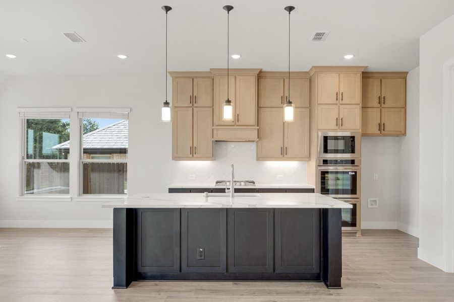 Kitchen with dark island, white countertops, light wood cabinets, pendant lights, and stainless steel double ovens Kitchen with dark island, white countertops, light wood cabinets, pendant lights, and stainless steel double ovens