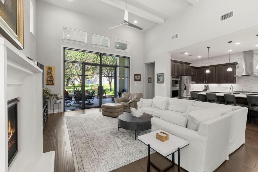 A spacious living room with soaring ceilings seamlessly transitions to a modern kitchen.