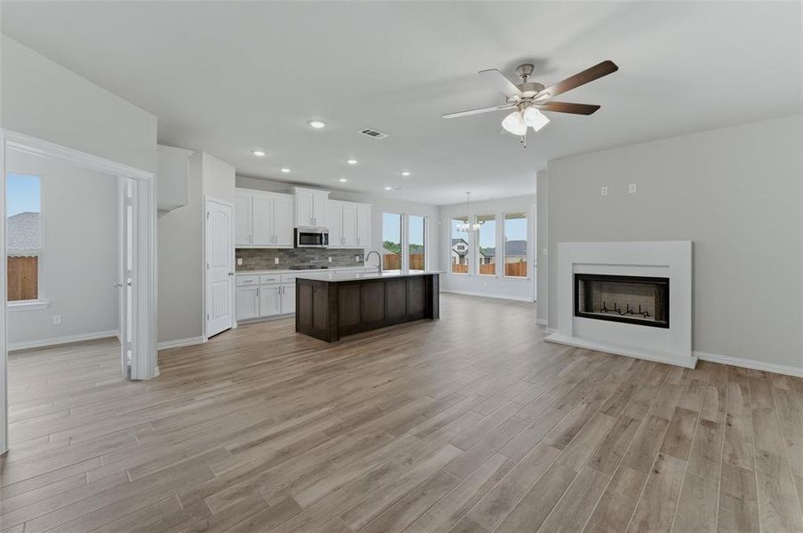 Spacious open-concept interior featuring light wood-finish flooring, a contemporary fireplace, and recessed lighting