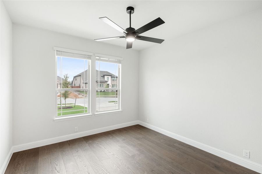 Empty bedroom with dark hardwood floors, white walls, ceiling fan, and two windows overlooking a neighborhood street. Empty bedroom with dark hardwood floors, white walls, ceiling fan, and two windows overlooking a neighborhood street.