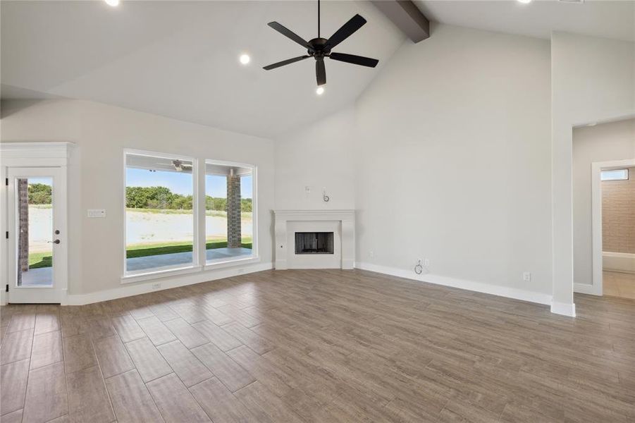 Unfurnished living room featuring a healthy amount of sunlight, beam ceiling, ceiling fan, and hardwood / wood-style flooring