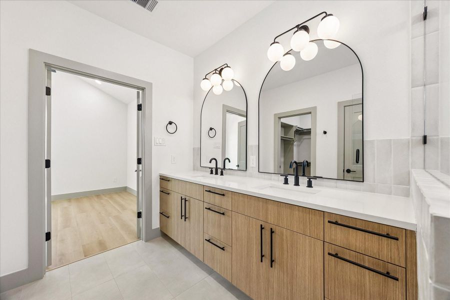 Warm wood cabinetry, dual quartz vanities, oversized arched mirrors, and matte black fixtures blend modern simplicity with everyday luxury. Warm wood cabinetry, dual quartz vanities, oversized arched mirrors, and matte black fixtures blend modern simplicity with everyday luxury.