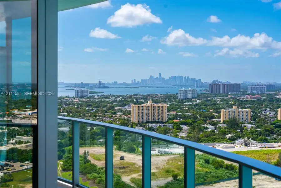 Expansive terrace with floor-to-ceiling glass paneling and a metal railing, providing a panoramic cityscape and water horizon Expansive terrace with floor-to-ceiling glass paneling and a metal railing, providing a panoramic cityscape and water horizon