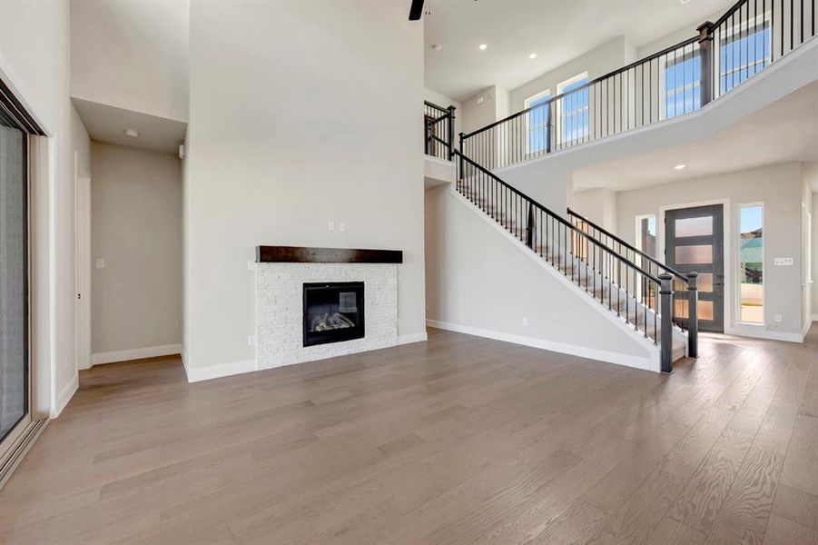 Unfurnished living room featuring wood finished floors, a high ceiling, a stone fireplace, and recessed lighting Unfurnished living room featuring wood finished floors, a high ceiling, a stone fireplace, and recessed lighting