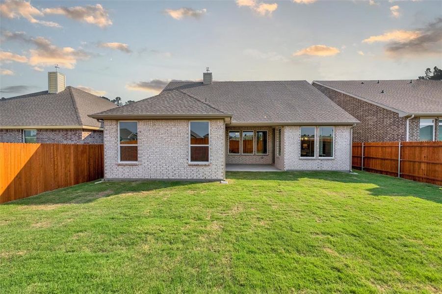 Back of house at dusk featuring a fenced backyard, a patio area, brick siding, and roof with shingles