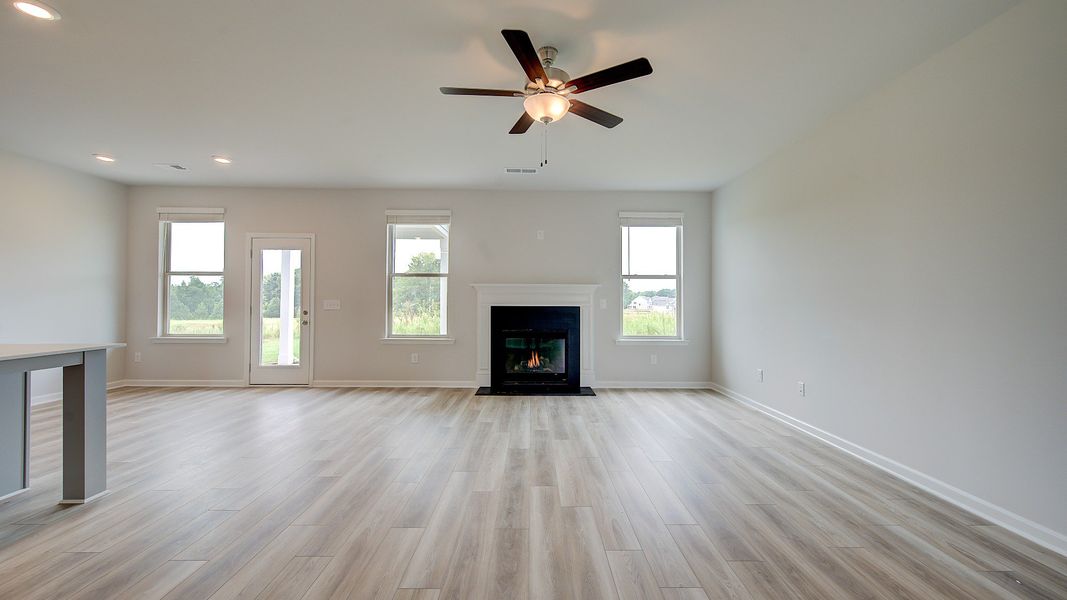 Meridian II family room with center gas fireplace, LVP flooring, and ceiling fan light at Brighton in Locust Grove, GA.