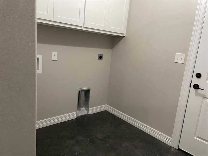 Washroom with dark tile patterned flooring, electric dryer hookup, and cabinets