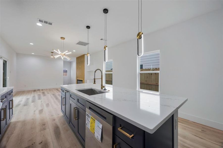 Kitchen with pendant lighting, sink, dishwasher, light stone counters, and a large island with sink