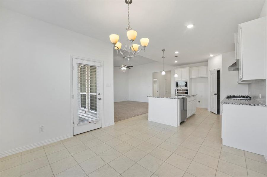 Kitchen with white cabinets, a kitchen island with sink, light stone countertops, and hanging light fixtures