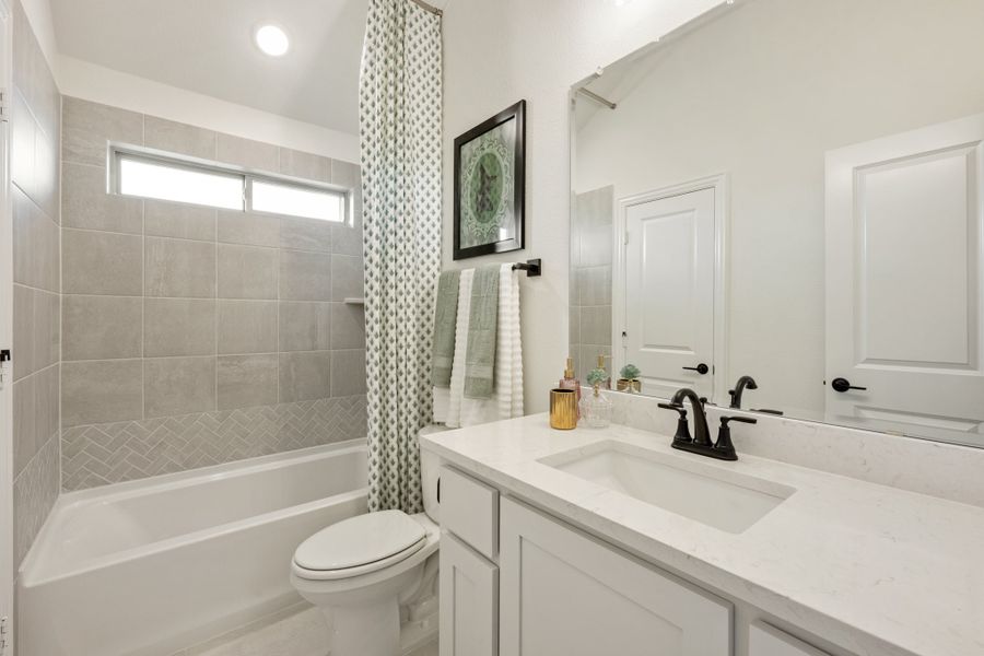 Bathroom with white vanity, tub-shower combo with gray tile surround, and large mirror