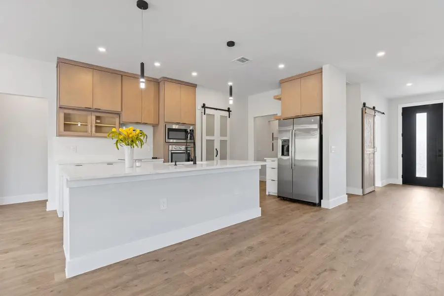 Kitchen with a barn door, appliances with stainless steel finishes, decorative light fixtures, recessed lighting, and light wood-style floors