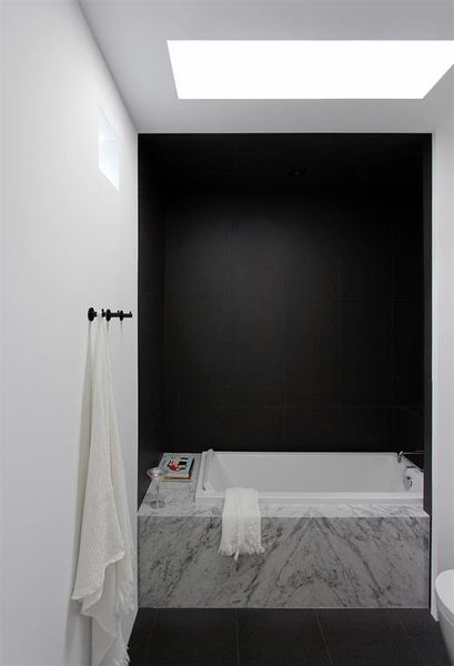 Guest bathroom includes a Duravit tub with headrest by Felipe Starke set on book-matched Carrera marble platform with a porcelain surround.