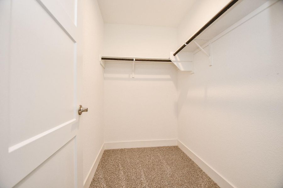 This photo features the secondary primary bedroom's spacious walk-in closet with clean white walls, carpeted flooring, and two sturdy hanging rods for ample storage. This photo features the secondary primary bedroom's spacious walk-in closet with clean white walls, carpeted flooring, and two sturdy hanging rods for ample storage.