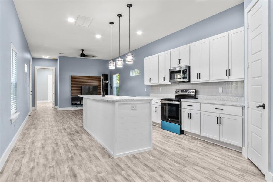 Kitchen with pendant lighting, appliances with stainless steel finishes, an island with sink, and white cabinets