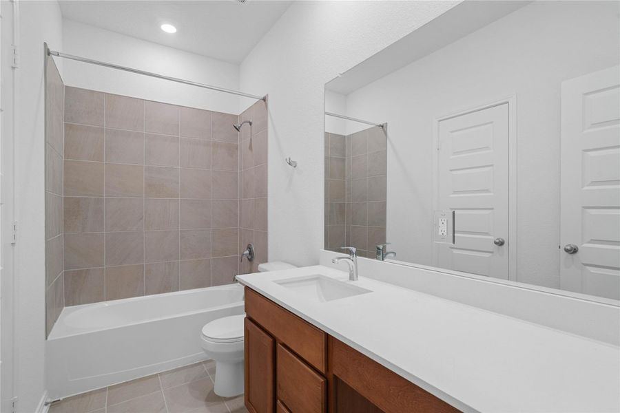 The secondary bathroom showcases tile flooring, a bath/shower combo with Daltile tile surround, a vanity with knee space and a stunning light countertop, large mirror, sleek fixtures, and contemporary finishes throughout. The secondary bathroom showcases tile flooring, a bath/shower combo with Daltile tile surround, a vanity with knee space and a stunning light countertop, large mirror, sleek fixtures, and contemporary finishes throughout.