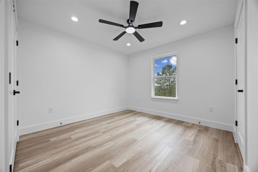 Bright interior space featuring wood-finish flooring, white walls, and a window with a tree-lined backdrop Bright interior space featuring wood-finish flooring, white walls, and a window with a tree-lined backdrop