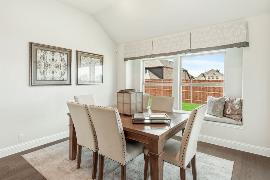 Dining room with wood table, cream upholstered chairs, window seat, and vaulted ceiling