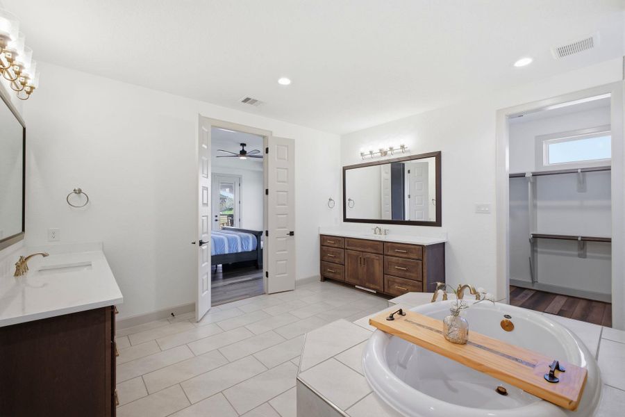 This spacious bathroom features light-colored tile flooring, a large soaking tub, and dual vanity areas with ample storage