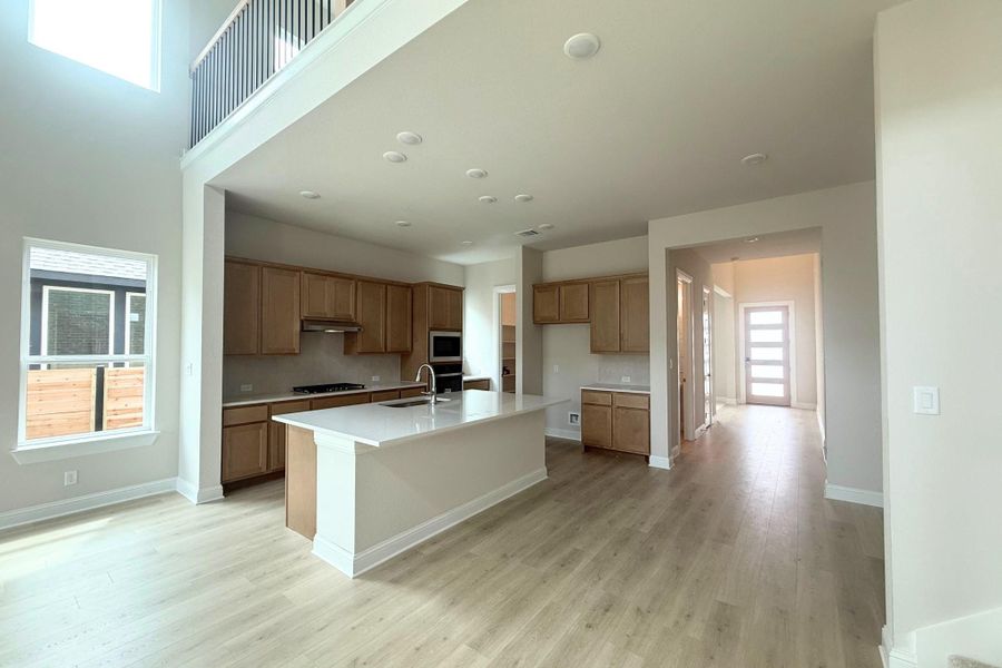 Open-concept living area featuring a two-story ceiling, wood-finish flooring, a kitchen island with a white countertop, light wood cabinetry, and recessed lighting throughout Open-concept living area featuring a two-story ceiling, wood-finish flooring, a kitchen island with a white countertop, light wood cabinetry, and recessed lighting throughout