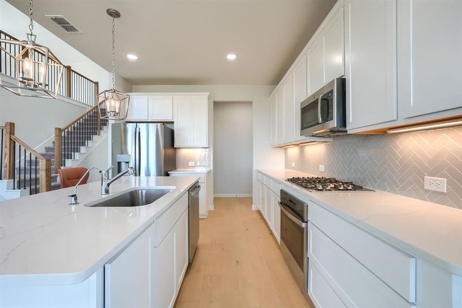 Kitchen featuring decorative light fixtures, tasteful backsplash, appliances with stainless steel finishes, light wood-type flooring, and light stone counters Kitchen featuring decorative light fixtures, tasteful backsplash, appliances with stainless steel finishes, light wood-type flooring, and light stone counters