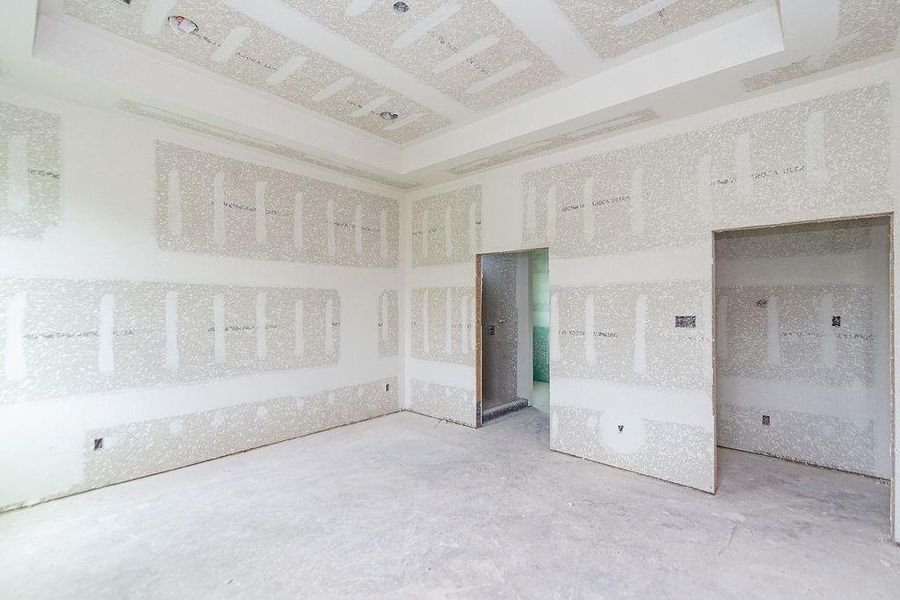 Spacious unfinished primary bedroom with drywall installation and ample natural light, offering a blank canvas for customization and personal design preferences. Spacious unfinished primary bedroom with drywall installation and ample natural light, offering a blank canvas for customization and personal design preferences.