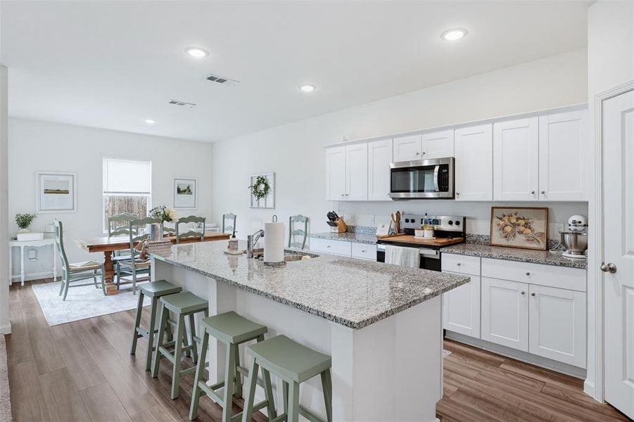 Kitchen island with a granite countertop, white shaker-style cabinetry, stainless steel appliances, wood-finish flooring, and recessed lighting