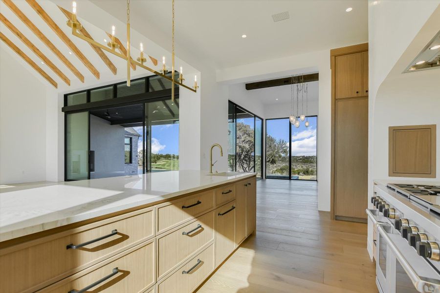 Kitchen featuring double oven range, light wood finish cabinets, light stone countertops, light wood-type flooring, and suspended lighting