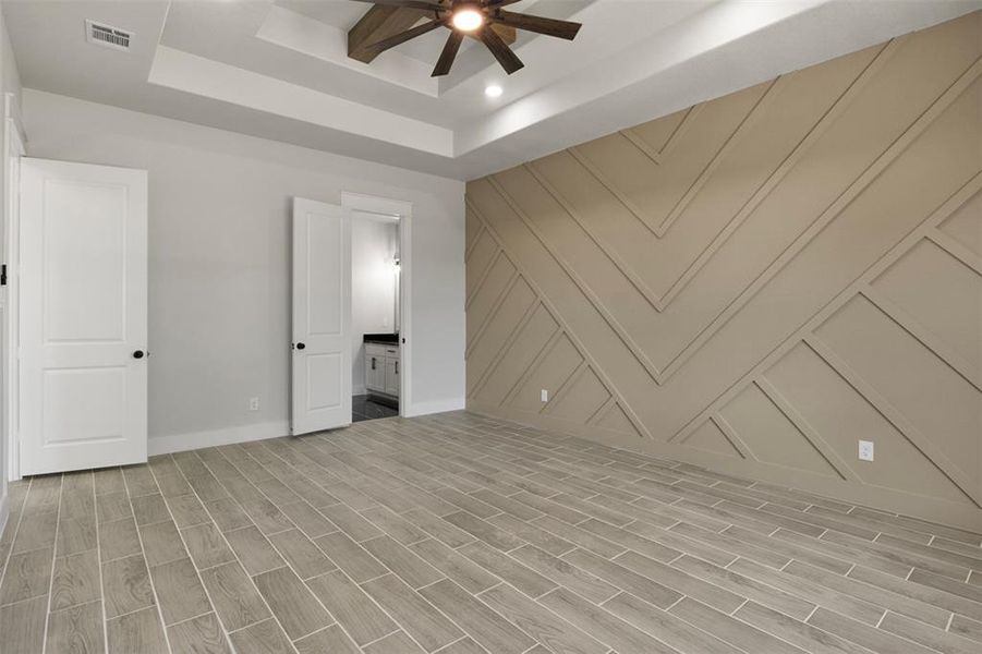 Unfurnished room featuring light wood-type flooring, ceiling fan, and a raised ceiling