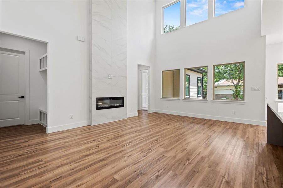 Unfurnished living room with a high ceiling, plenty of natural light, a premium fireplace, and wood-type flooring