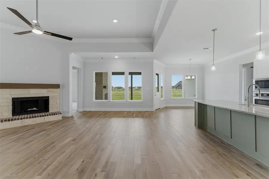 Open-concept living space featuring wood-finish flooring, a stone fireplace with a wood mantle, and a contemporary ceiling fan