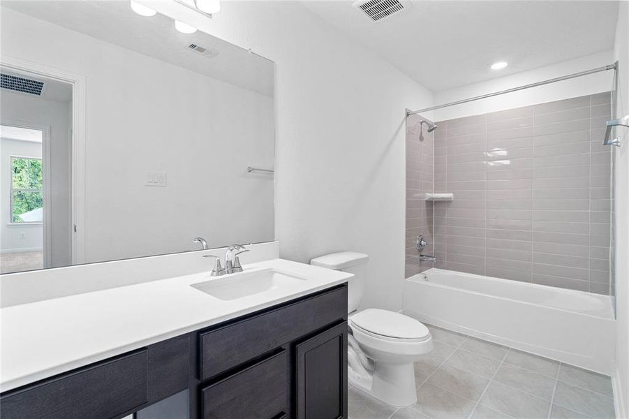 Secondary bath features tile flooring, bath/shower combo with tile surround, stained wood cabinets, beautiful light countertops, mirror, sleek fixtures and modern finishes.