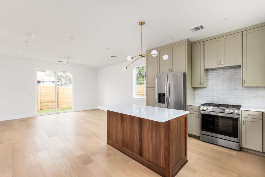 Kitchen featuring stainless steel appliances, light wood-type flooring, decorative backsplash, hanging light fixtures, and open floor plan
