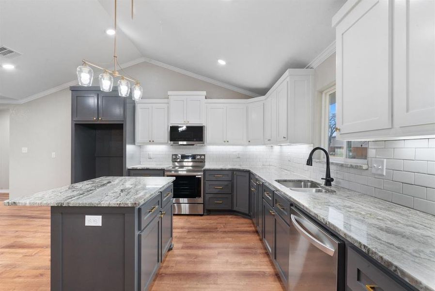 Kitchen featuring stainless steel appliances, sink, a center island, white cabinetry, and lofted ceiling Kitchen featuring stainless steel appliances, sink, a center island, white cabinetry, and lofted ceiling