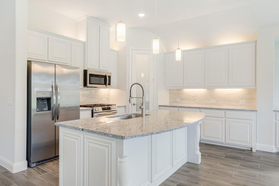 Kitchen with white cabinets, granite island, stainless steel appliances, and pendant lights above the sink.