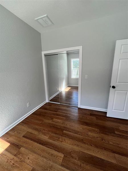 Unfurnished bedroom with a textured wall, dark wood-type flooring, a closet, and a textured ceiling Unfurnished bedroom with a textured wall, dark wood-type flooring, a closet, and a textured ceiling