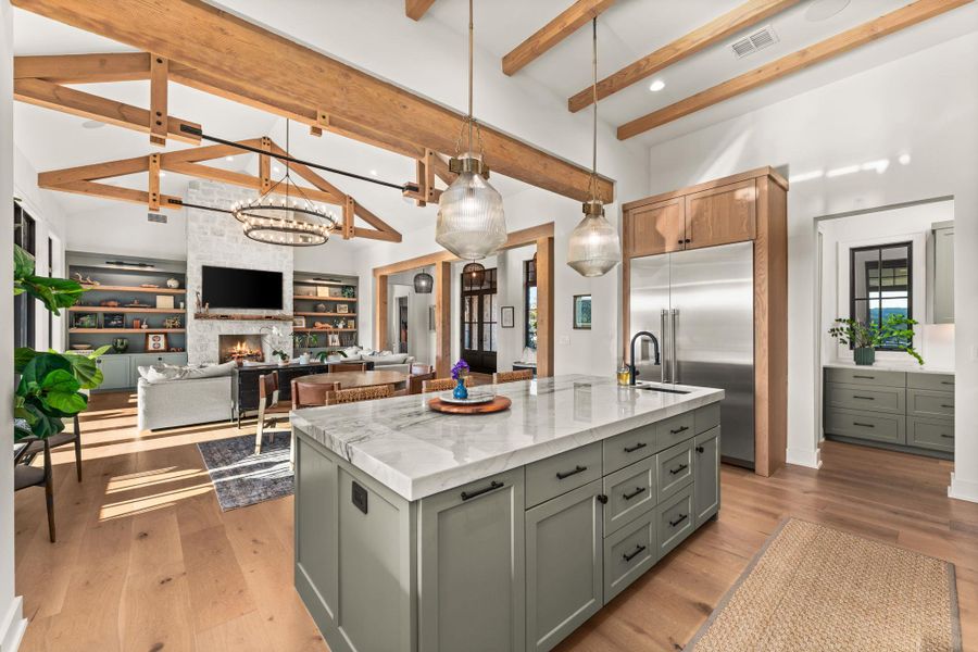 Kitchen with decorative light fixtures, a large fireplace, a chandelier, stainless steel built in fridge, and an island with sink Kitchen with decorative light fixtures, a large fireplace, a chandelier, stainless steel built in fridge, and an island with sink