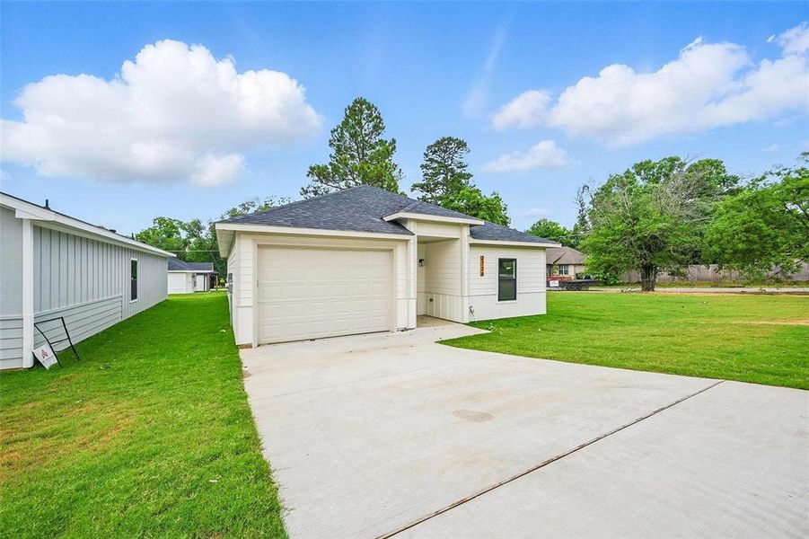 View of front of home featuring a front yard, driveway, roof with shingles, and an attached garage