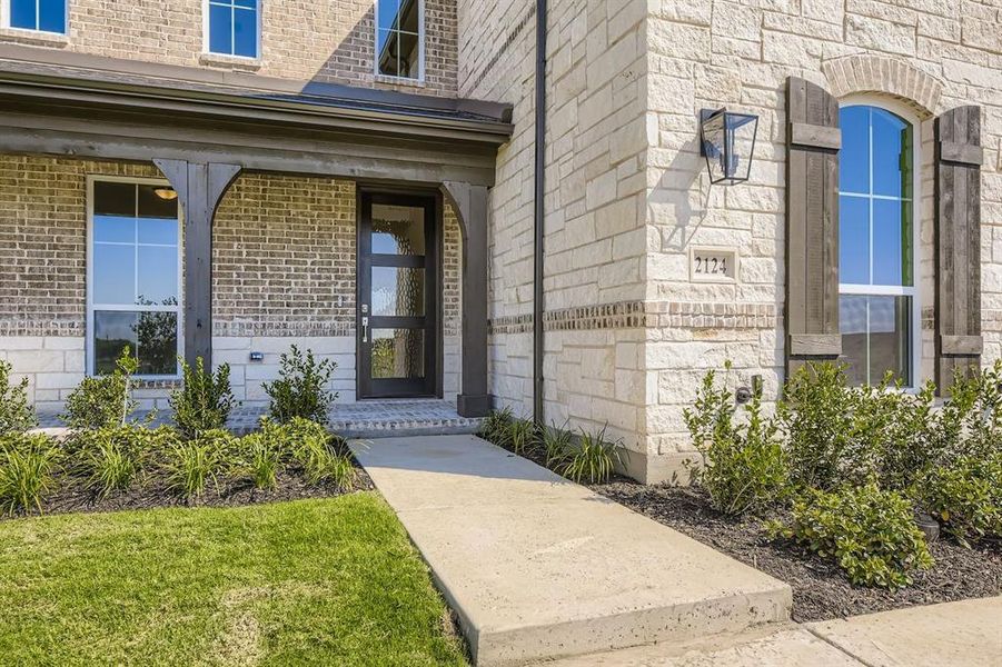 Entrance to property featuring stone siding, covered porch, and brick siding
