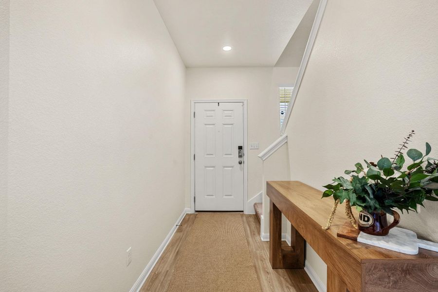 Enter into a welcoming hallway, featuring warm wood-look flooring leading to the main entrance.