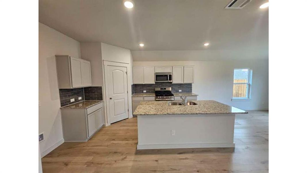 Contemporary kitchen featuring light wood-finish flooring, white cabinetry, granite countertops, and a gray subway tile backsplash