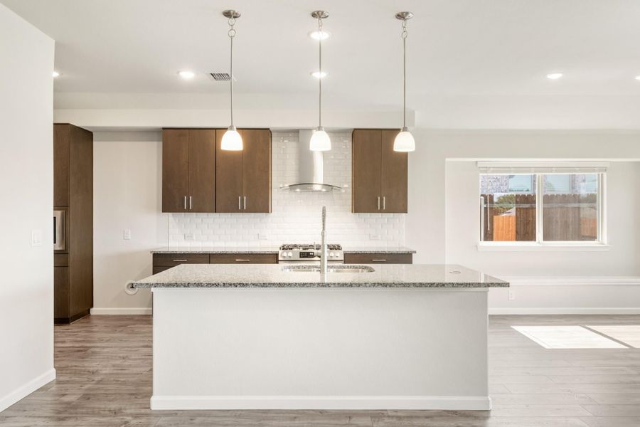 Kitchen with large island, granite countertop, dark wood cabinets, white tile backsplash, and three pendant lights