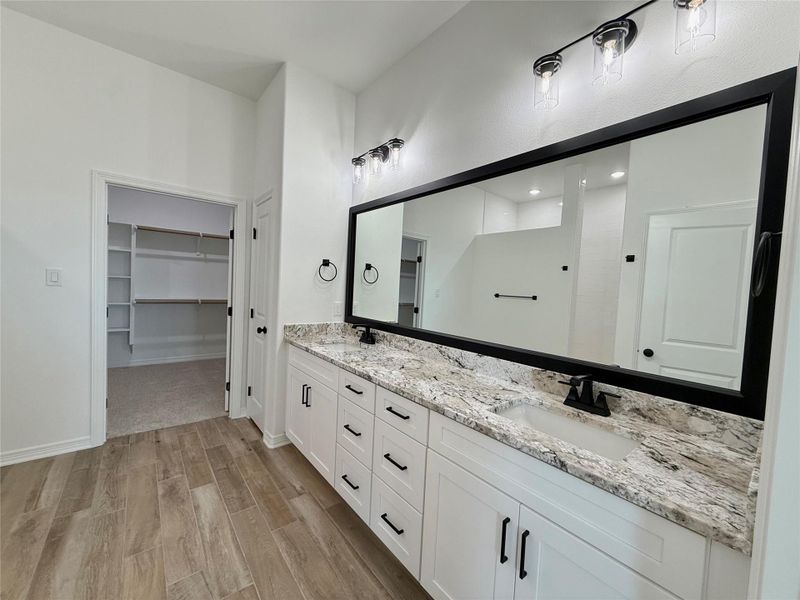 Dual vanity with white cabinetry and dark hardware, granite countertops, and wood-finish flooring