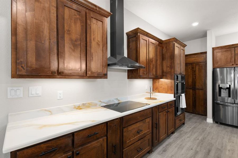Kitchen featuring black appliances, wall chimney range hood, and light wood-style floors