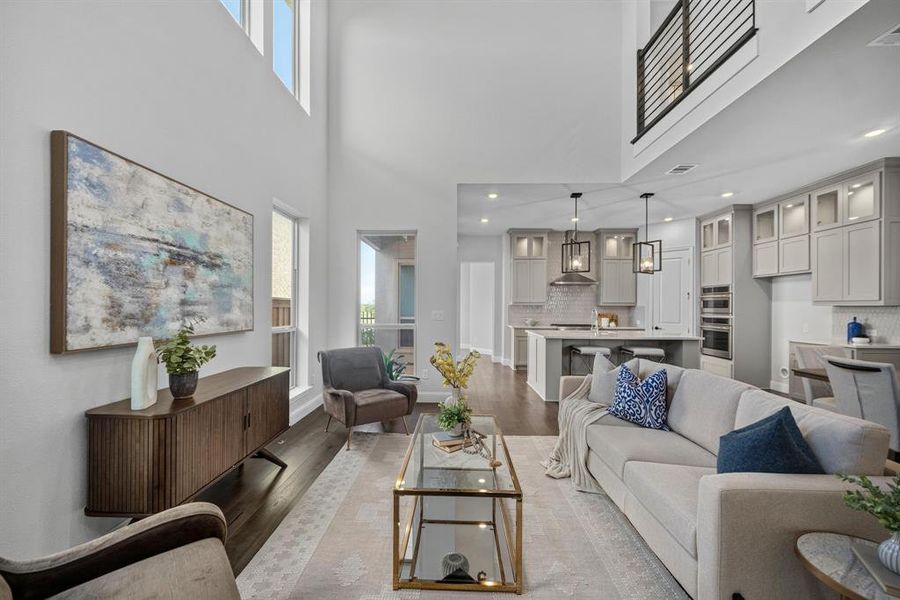 Open-concept living area featuring high ceilings, wood-finish flooring, a modern kitchen with light cabinetry, a kitchen island with seating, and a second-story interior balcony with metal railing