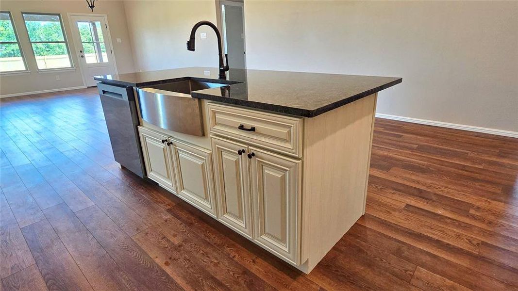 Kitchen with dishwasher, dark wood-style floors, an island with sink, cream cabinets, and dark stone counters