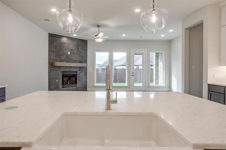 Kitchen with a tile fireplace, ceiling fan, sink, decorative light fixtures, and a kitchen island