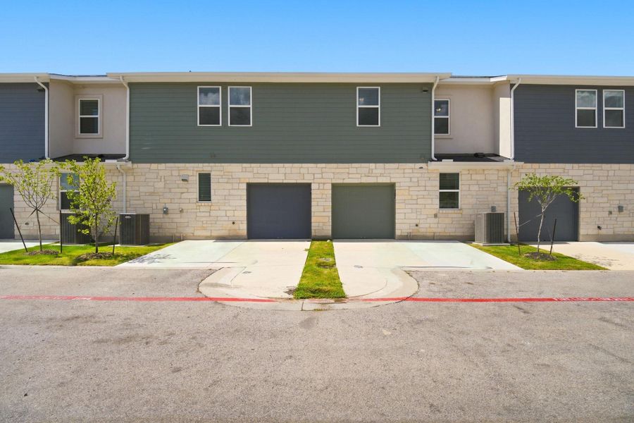 A modern multi-family exterior displays mixed stone and siding facade detailing above concrete driveways.