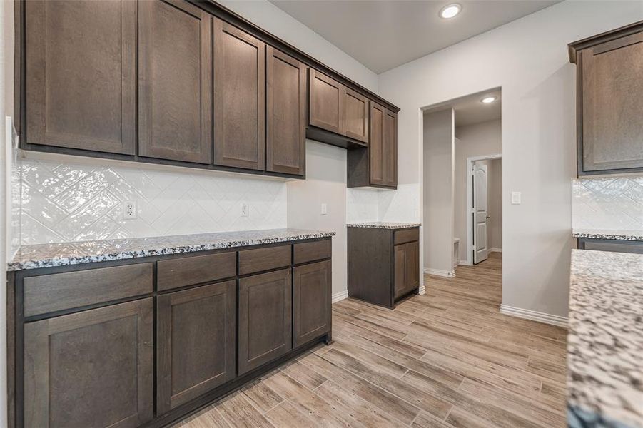 Kitchen with tasteful backsplash, light stone counters, dark brown cabinetry, recessed lighting, and light wood-style floors Kitchen with tasteful backsplash, light stone counters, dark brown cabinetry, recessed lighting, and light wood-style floors